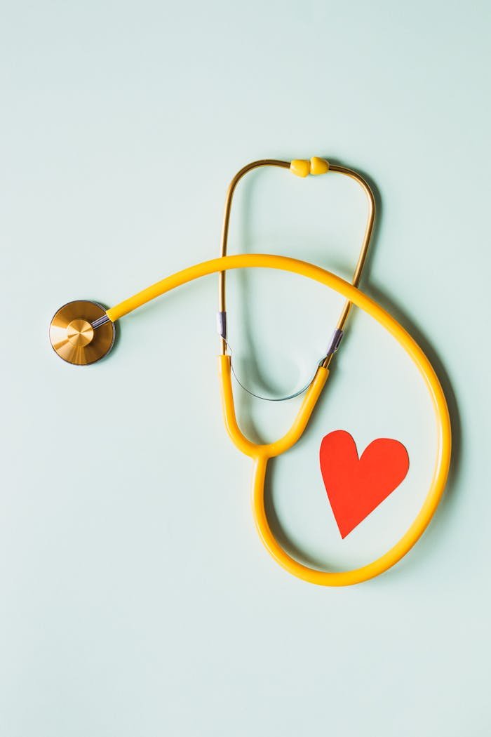 Home Yellow stethoscope arranged with a red heart cutout on a light green background, symbolizing heart health.