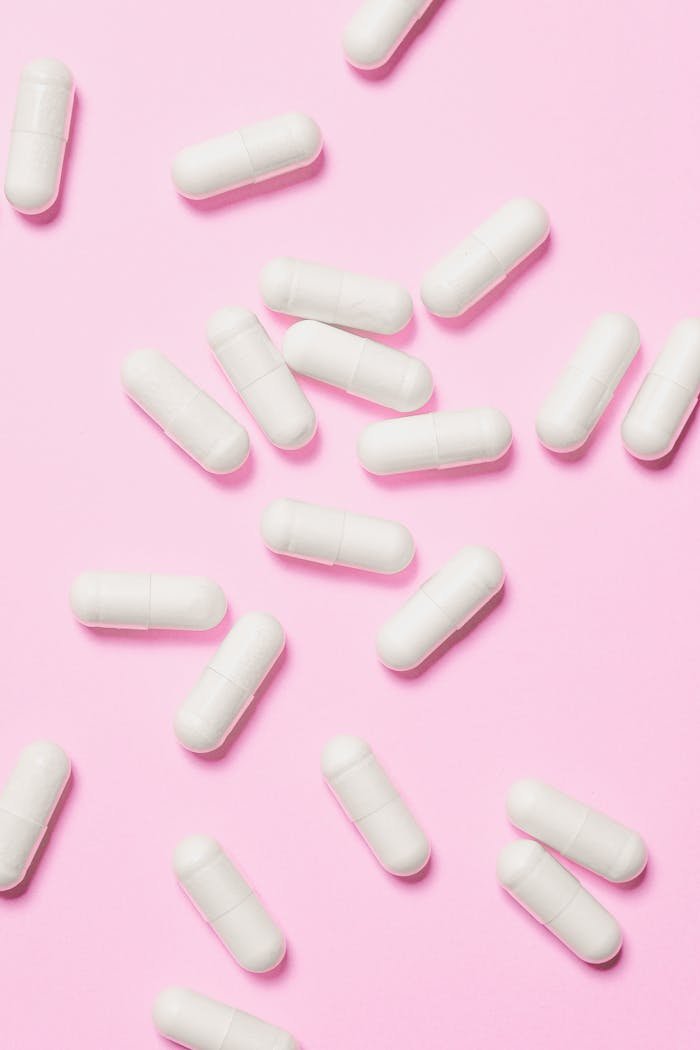 Home White medicinal capsules scattered on a vibrant pink background, symbolizing healthcare and wellness.